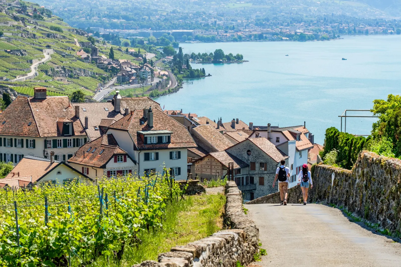 Deux promeneurs sur un chemin entre les vignes et un village du Lavaux, au-dessus du lac Léman