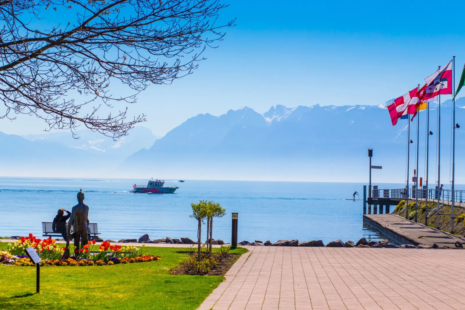 Promenade fleurie au bord du lac Léman à Saint-Sulpice, avec un bateau et les montagnes en arrière-plan