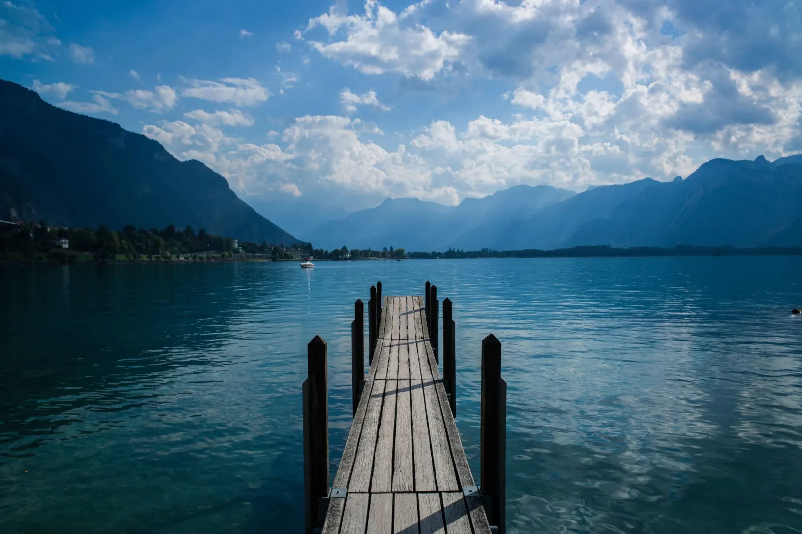 Ponton en bois avançant sur le lac Léman, avec les montagnes et un ciel nuageux en arrière-plan